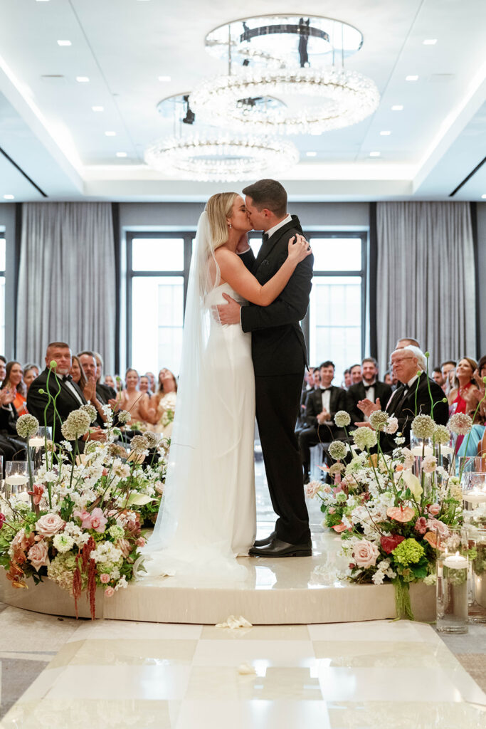 The couple exchanging vows during a beautiful outdoor ceremony, with the bride in her wedding gown and the groom in a classic suit, surrounded by nature and their closest family and friends.