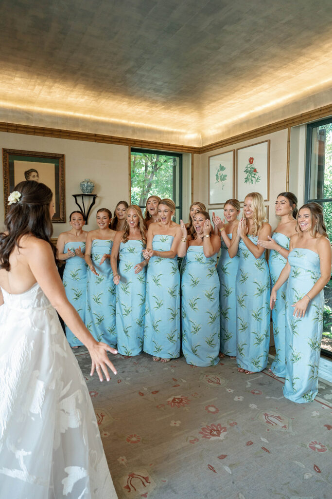 Bridesmaids in matching floral gowns revealing the bride of a romantic spring wedding.