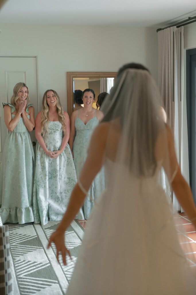 Bride laughing with bridesmaids dressed in pastel yellow while getting ready for the wedding morning.