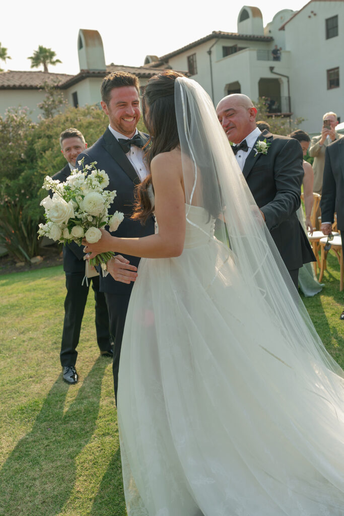 Bride and groom exchange vows on the lawn overlooking the ocean at The Ritz-Carlton Bacara, surrounded by elegant floral arrangements.
