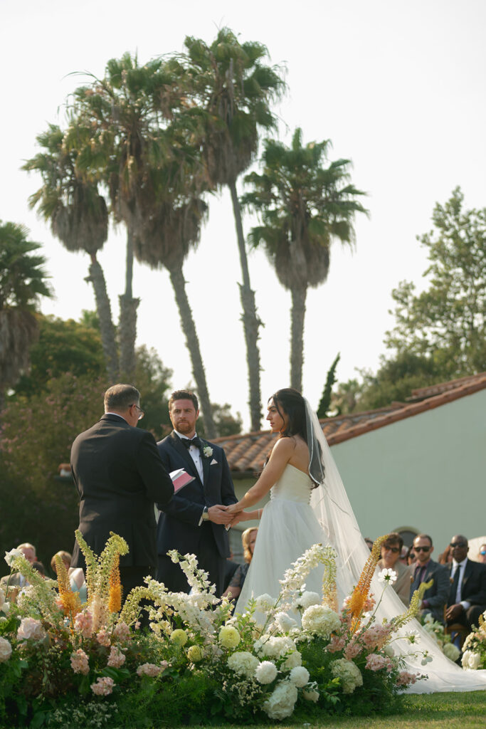 Bride and groom exchange vows on the lawn overlooking the ocean at The Ritz-Carlton Bacara, surrounded by elegant floral arrangements.