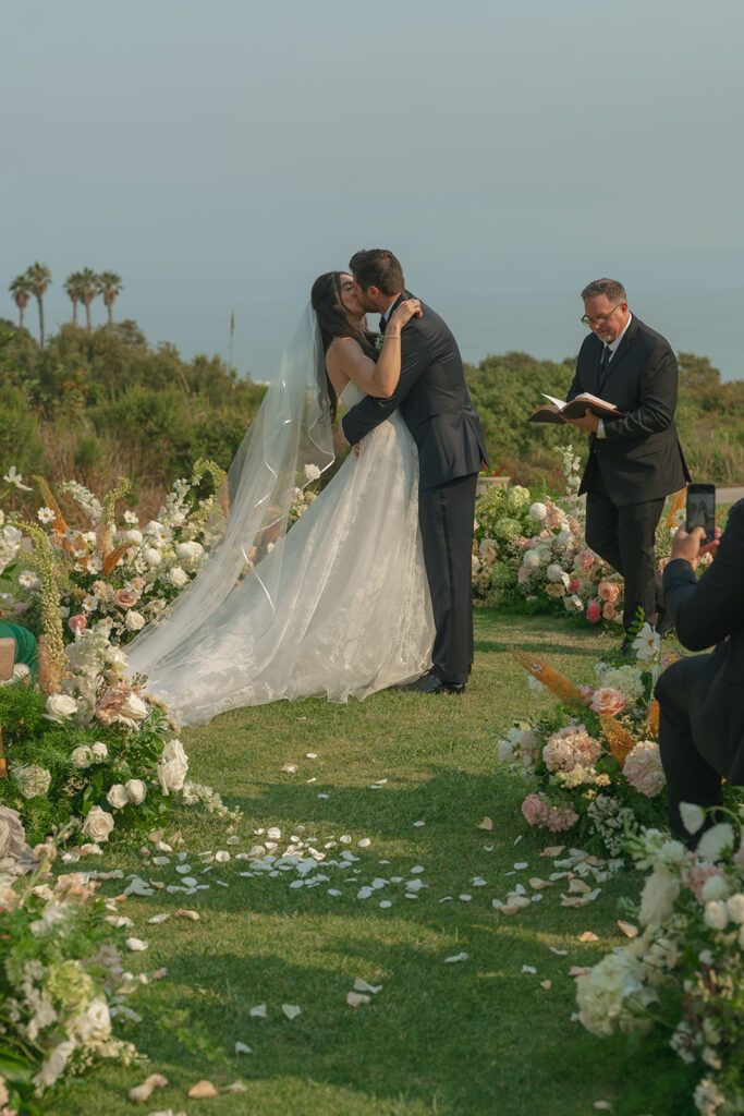 Bride and groom exchange vows on the lawn overlooking the ocean at The Ritz-Carlton Bacara, surrounded by elegant floral arrangements.
