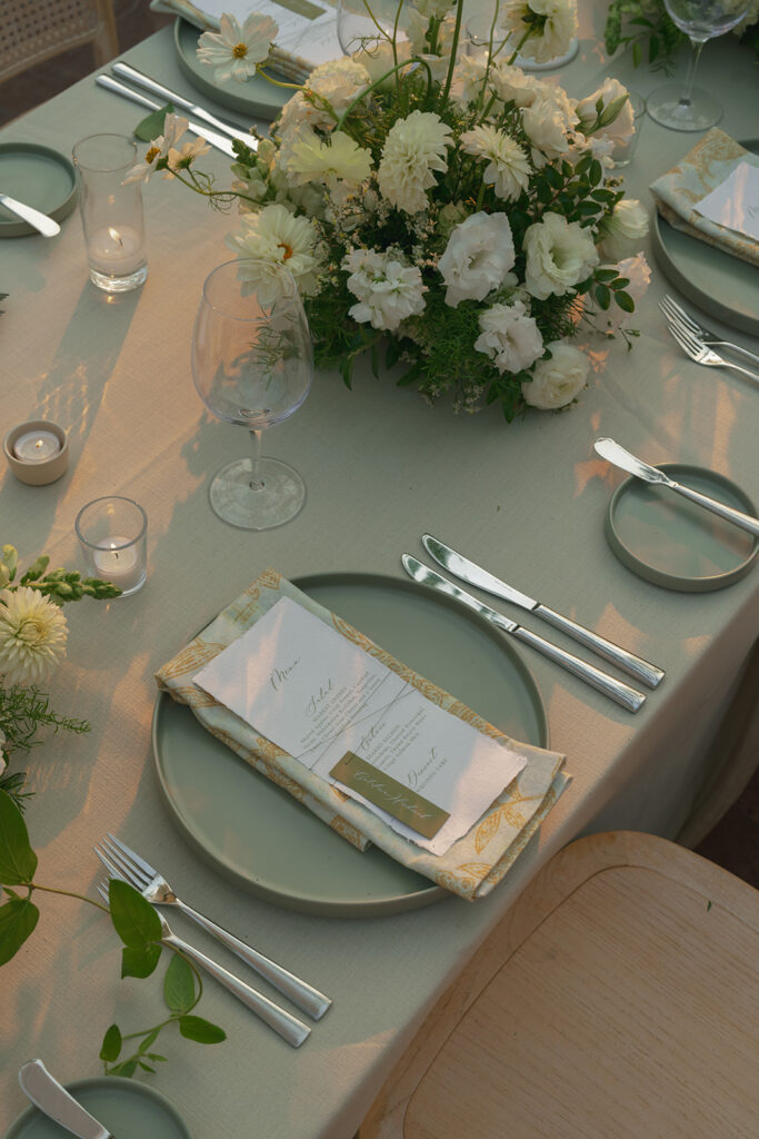 Reception tables at The Ritz-Carlton Bacara with soft white florals, candlelight, and crystal chandeliers glowing at sunset.