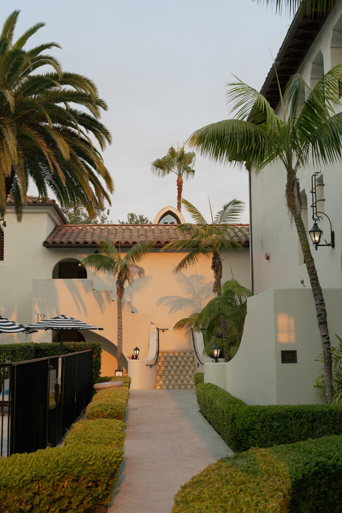 Reception tables at The Ritz-Carlton Bacara with soft white florals, candlelight, and crystal chandeliers glowing at sunset.