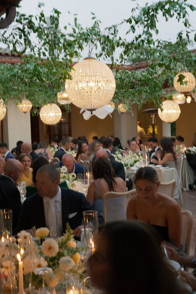 Reception tables at The Ritz-Carlton Bacara with soft white florals, candlelight, and crystal chandeliers glowing at sunset.