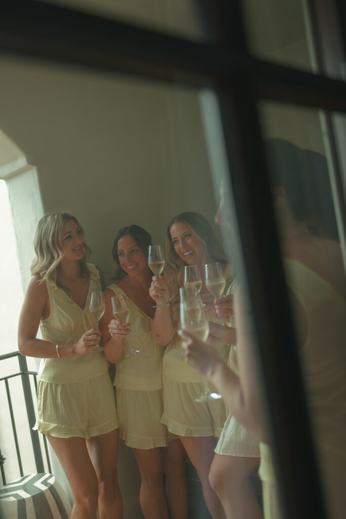 Bride laughing with bridesmaids dressed in pastel yellow while getting ready for the wedding morning.