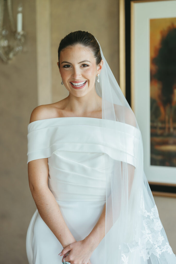 Bride getting ready for a classic Texas country club wedding wearing an off-the-shoulder gown and veil in a refined bridal suite