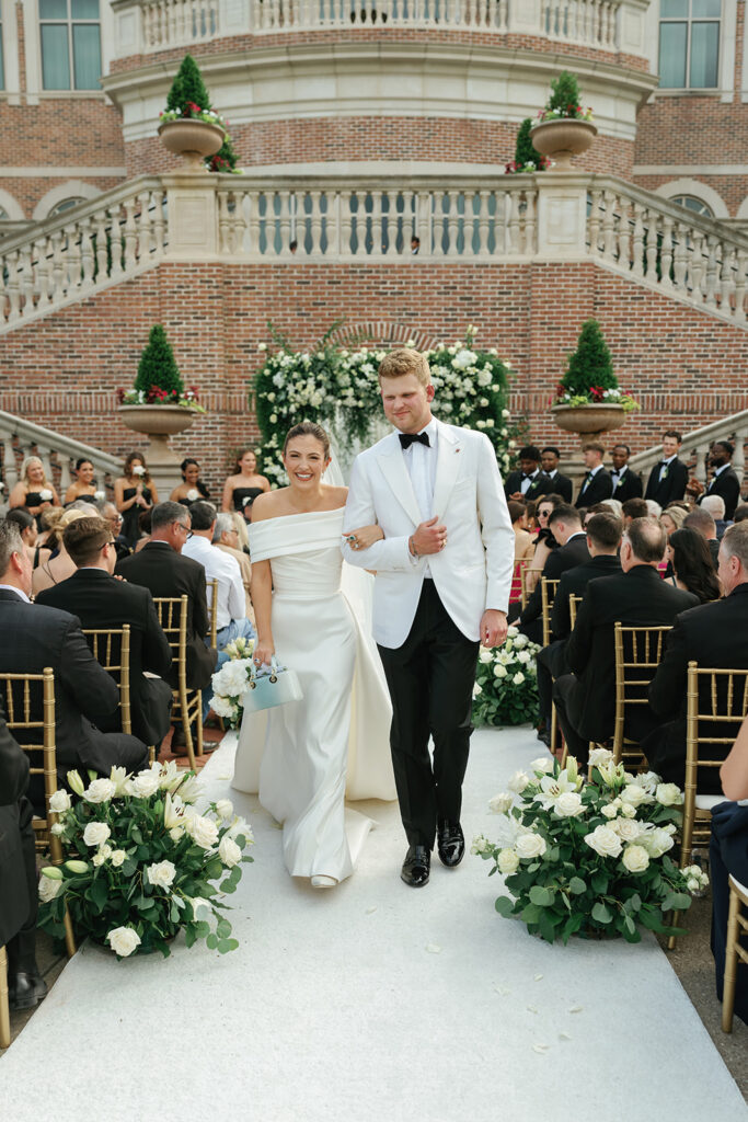 Bride and groom sharing their first kiss during a classic Texas country club wedding ceremony beneath an elegant white and green floral arch